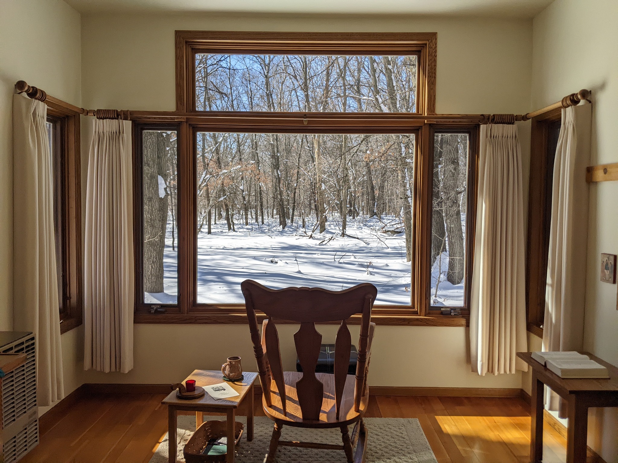Empty wooden char facing a bright window surrounded by curtains looking out to a snowy scene.