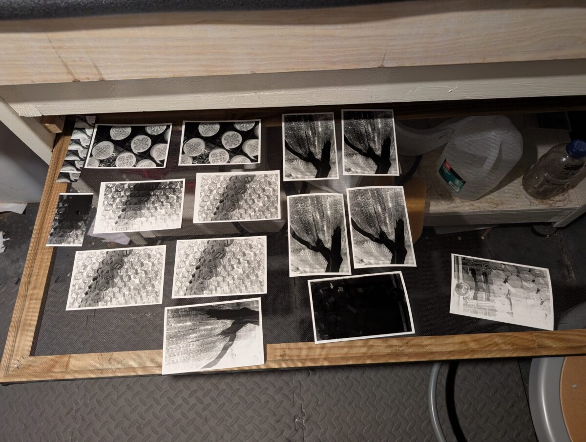 This black and white photo shows a variety of test prints and photographic prints resting on a window screen in a darkroom. These photos were taken at Jogyesa Temple in Seoul, South Korea.