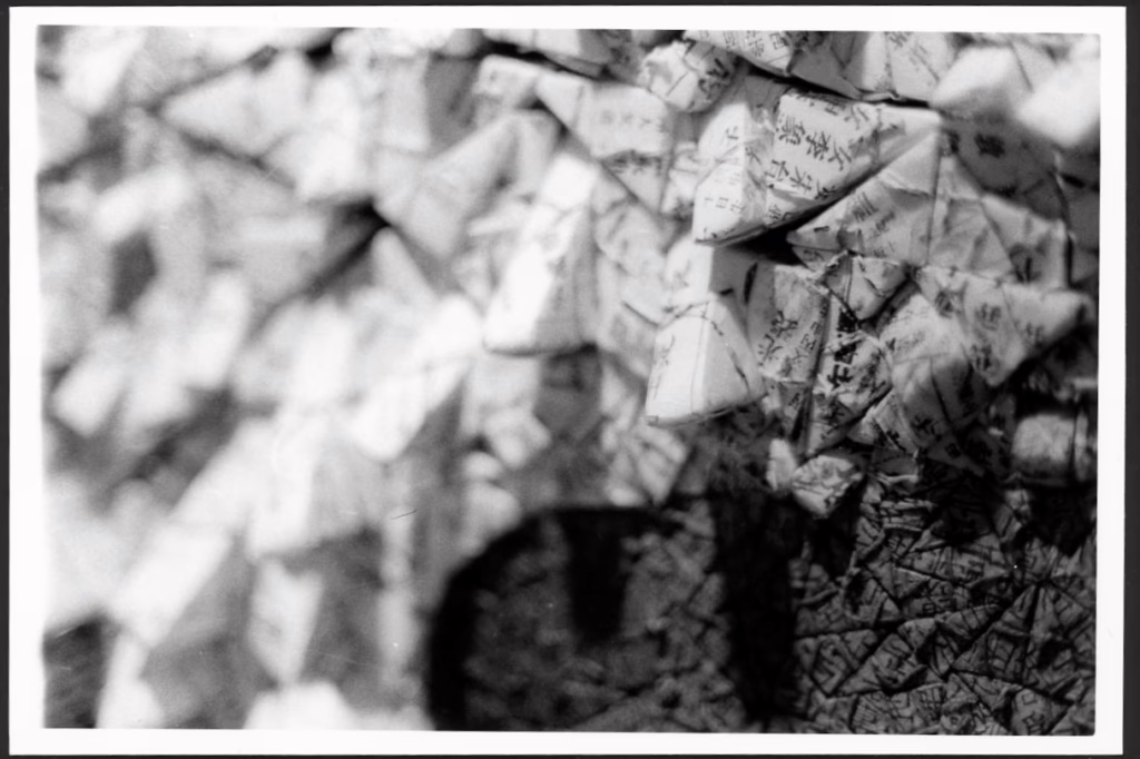 This black and white photograph sows traditional Korean paper (hanji) folded into different shapes and put next to each other. This creates a three-dimensional image that sticks out from the paper. You can also see writing on the shapes.