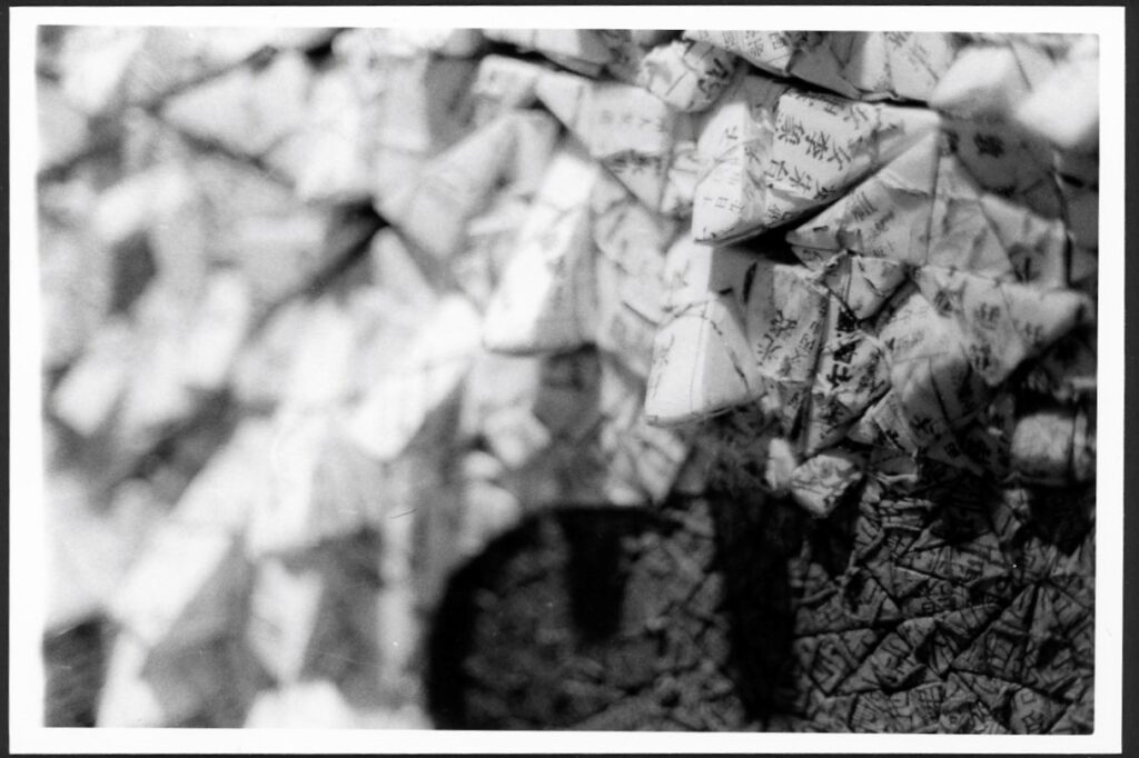 This black and white photograph sows traditional Korean paper (hanji) folded into different shapes and put next to each other. This creates a three-dimensional image that sticks out from the paper. You can also see writing on the shapes.