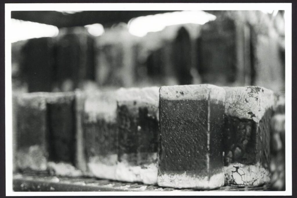 This black and white photograph shows rows of bricks on industrial shelving. The edges of the bricks appear pale and burnt compared to the center of the bricks.