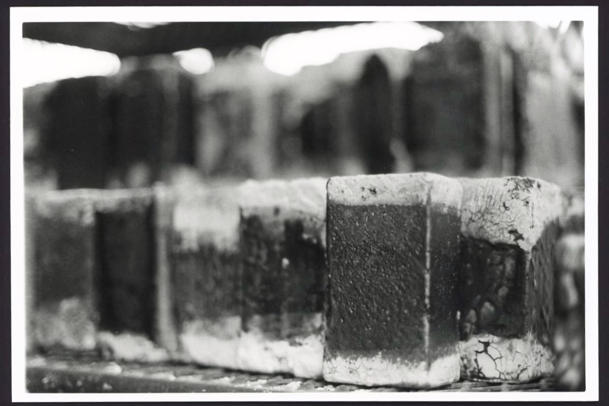 This black and white photograph shows rows of bricks on industrial shelving. The edges of the bricks appear pale and burnt compared to the center of the bricks.