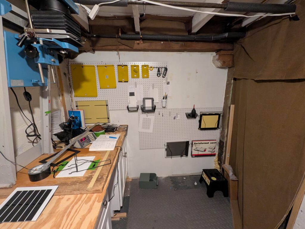 This photo shows a photographic darkroom in a basement. Heavy brown canvas curtains help block off light. If you look closely, you can also see spray foam near a wall in the far corner.