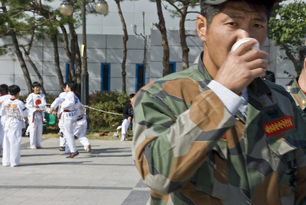 A Republic of Korea Marine looks at the camera while some kids in taekwondo uniforms play in the background.