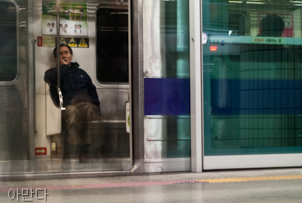 A man rests his head on the subway in South Korea. The subway train door is open and the faint image of people's legs can be seen from people who exited the subway.