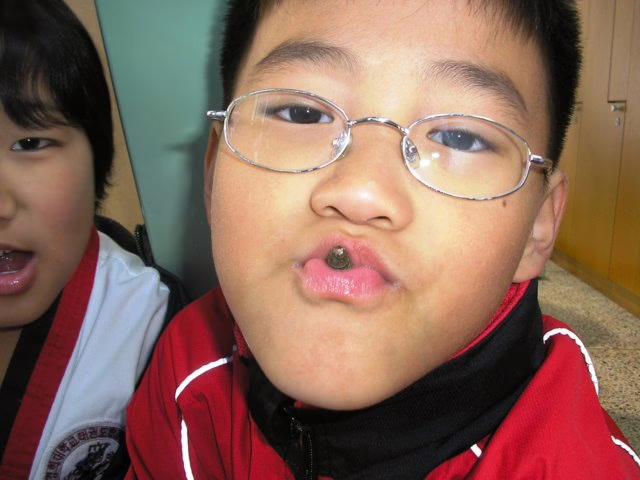 Two young boys sit in taekwondo uniforms. One of them sucks on a snail snack.