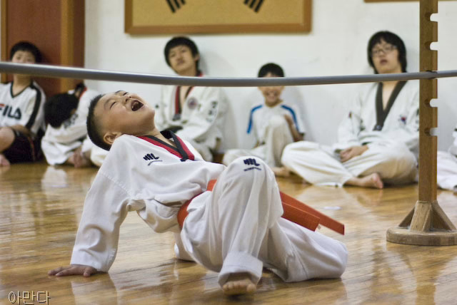 A young boy in a takewondo uniform limbos while others look on.