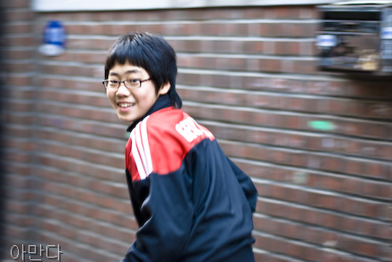 A boy wearing a red and black coat runs away smiling.