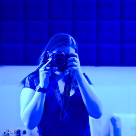 A self portrait, taken in a room bathed in blue light. I'm facing a mirror, and my face is obscured by my camera.