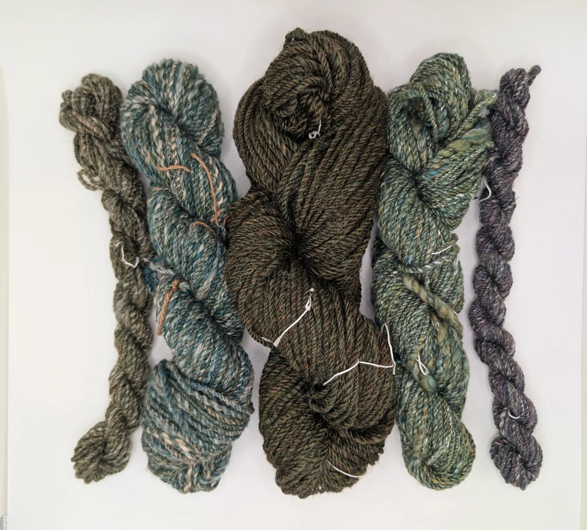 Five hanks of yarn, mostly in shades of green and blue, are shown on a white background.
