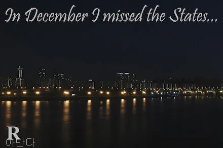 A nighttime scene features buildings in Seoul as seen behind the Han River, which is peppered with lights. A letter R is seen in the corner of this postcard.
