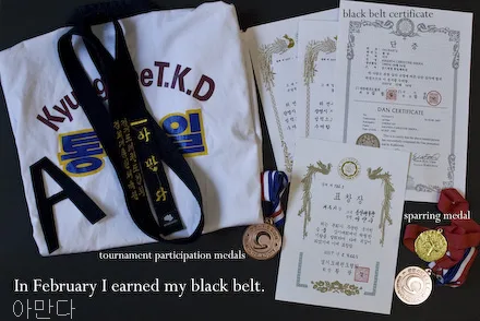 A taekwondo uniform and black belt are shown, along with several certificates and some medals. The letter A can be seen in the photo.