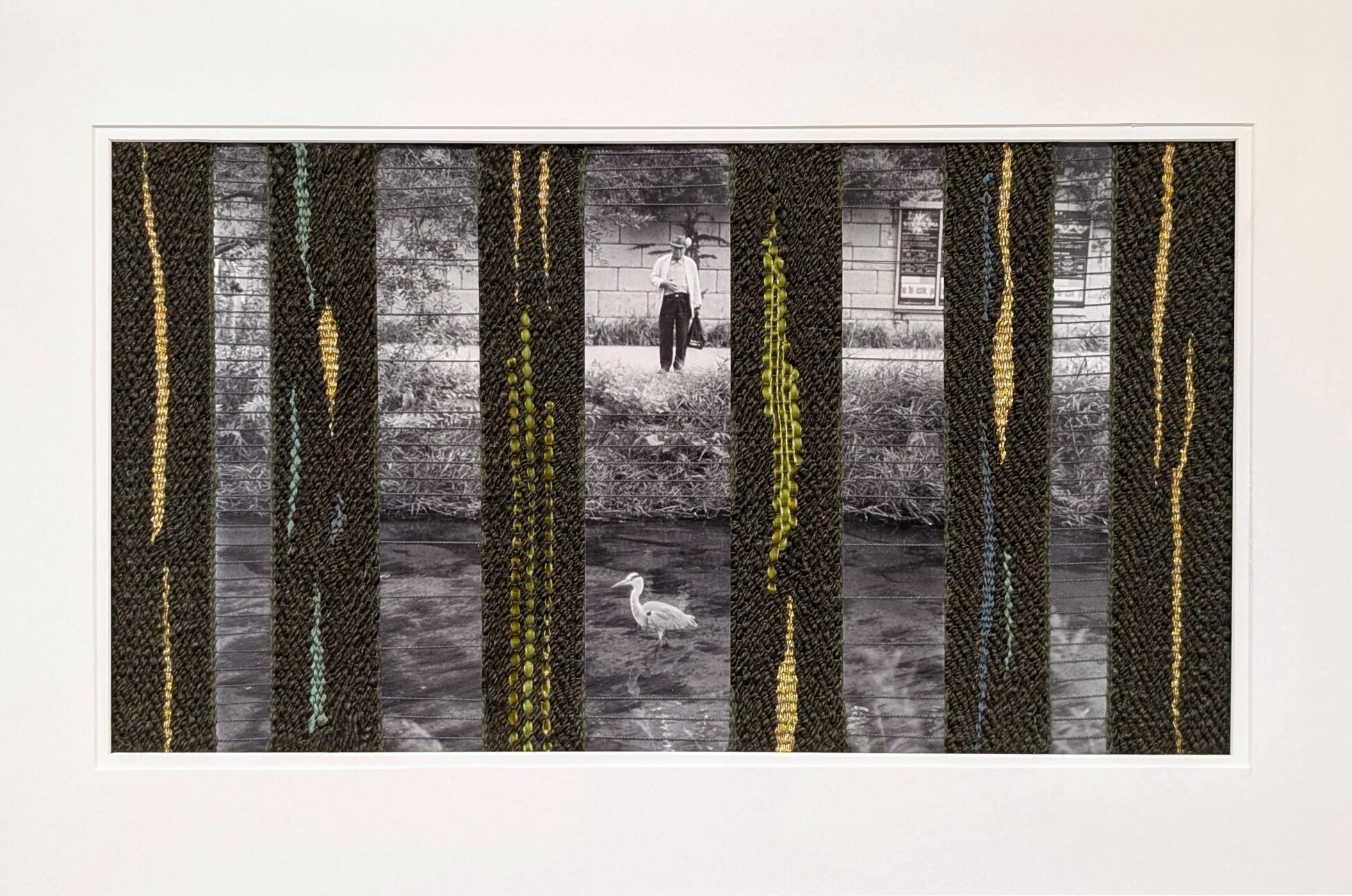 Grandfather and the Heron is a piece of woven textile art. Strips of photographic paper, which show a grandfather standing near a stream looking at a heron in the water, are woven with olive green yarn, strips of silk ribbon in greens and blues, velvet ribbon in two shades of green, and metallic gold embroidery floss.