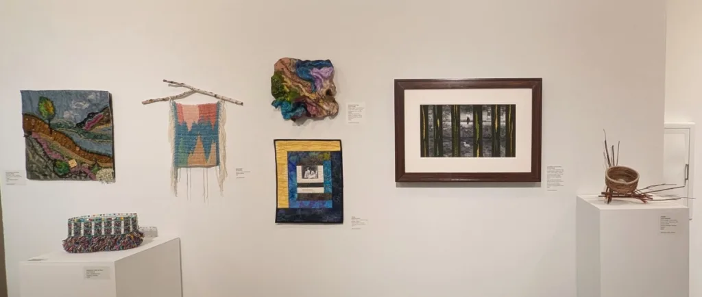 Seven pieces of artwork, including wall hangings, quilts, tapestry weavings, and basketry works, are shown in a gallery setting.