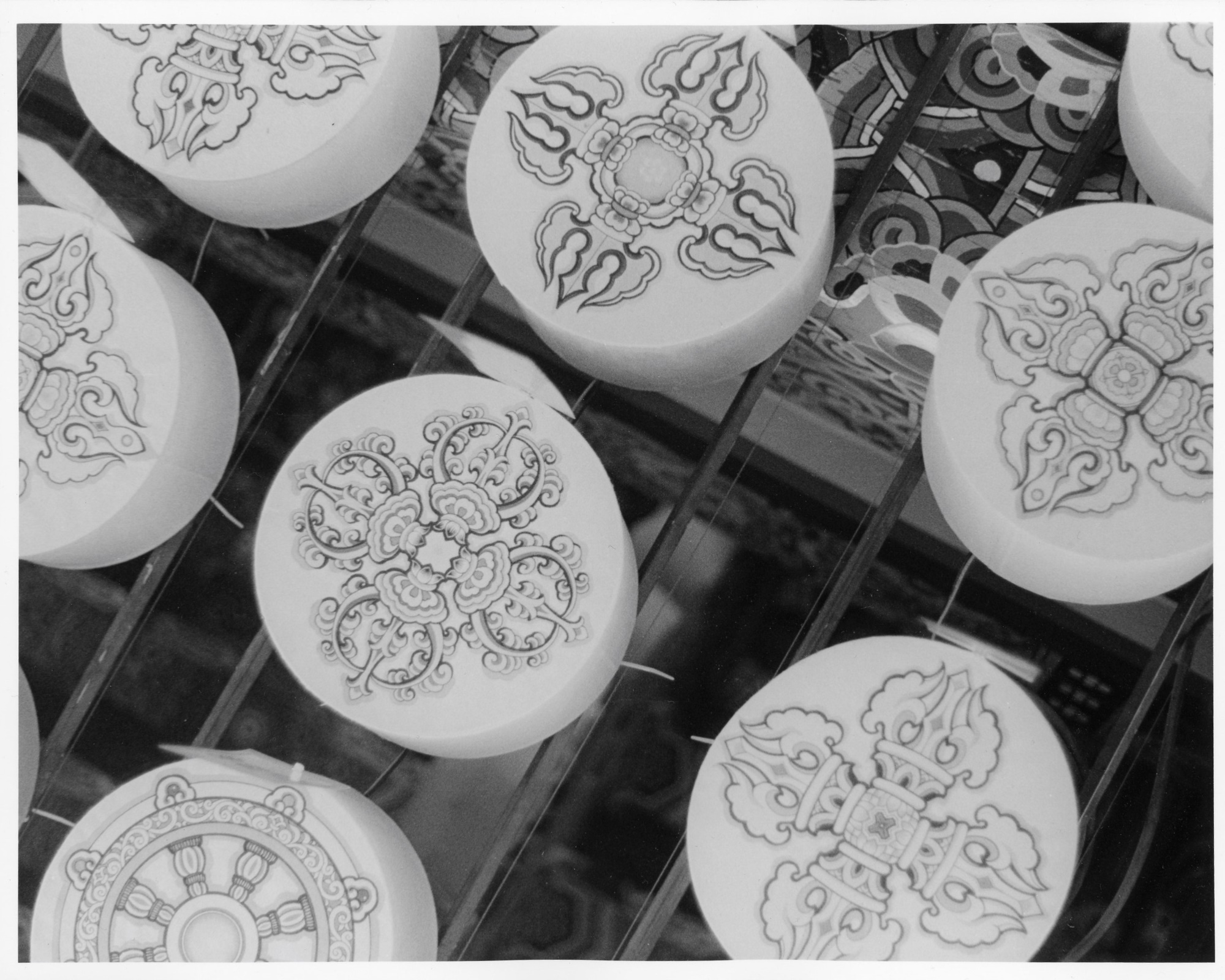 This black-and-white photo shows the flat bottom of some lanterns at Buddha's birthday parade in Seoul, South Korea in May 2024. Some ornate illustrations can be seen on each lantern. In the background, you can see the painting present on the underside of the roof of the temple.