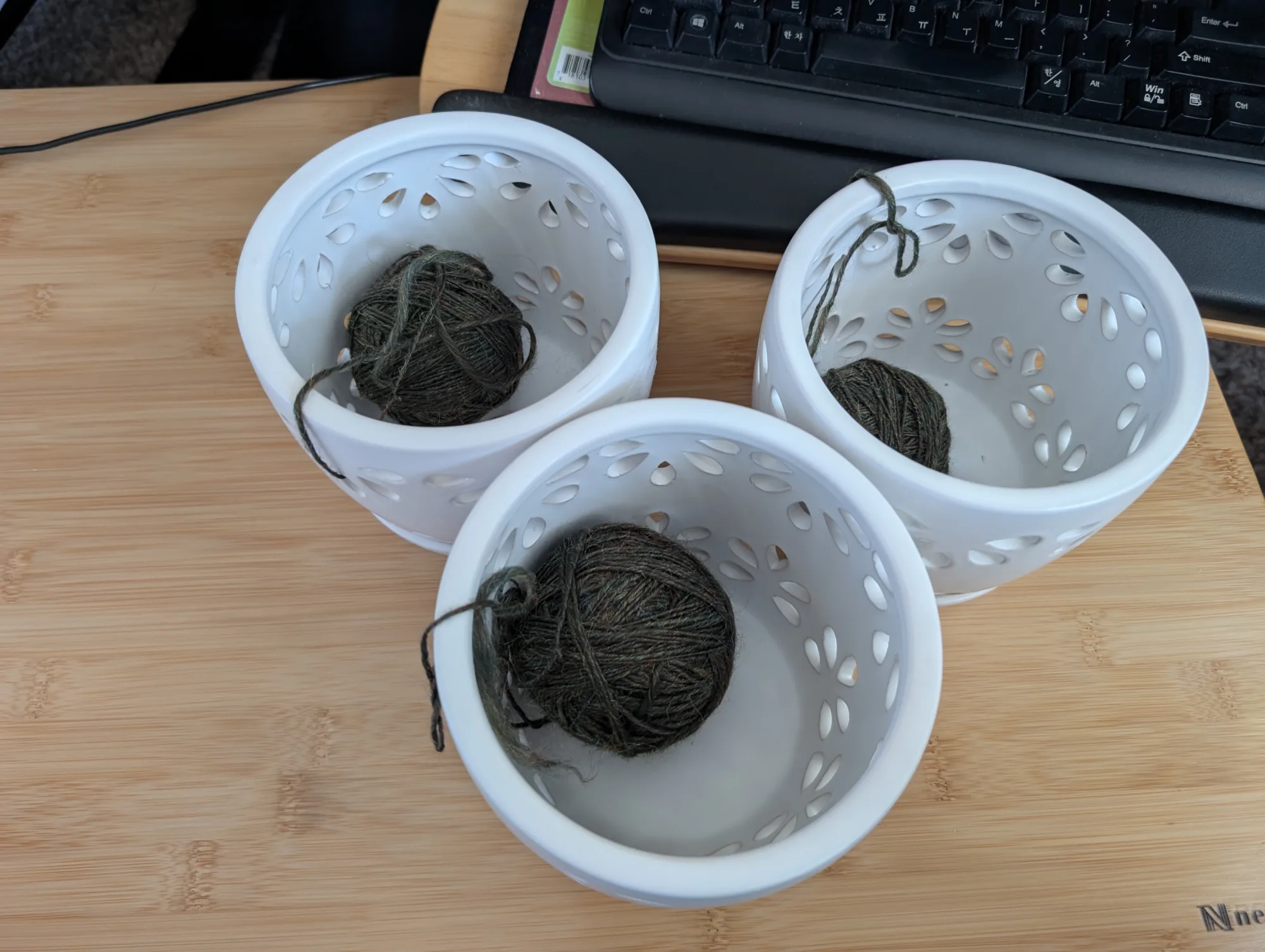Three small orchid pots are shown on a desk. Inside each pot is a small ball of green yarn.