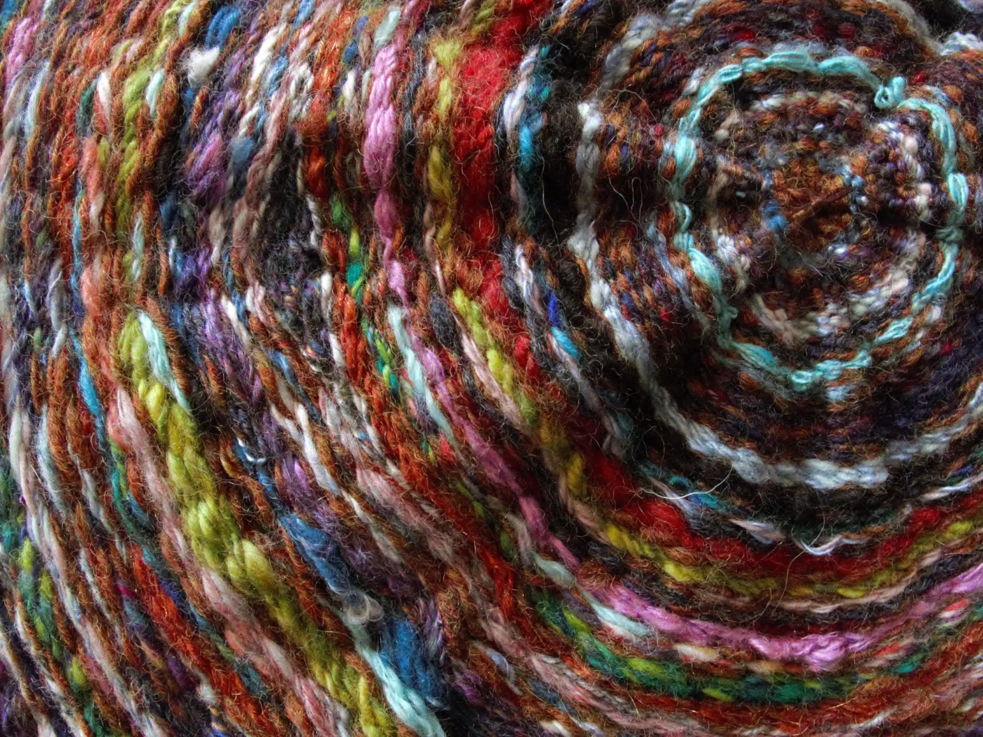 This close-up photo shows part of a piece of textile art. A variety of yarn colors are woven in a circular shape. The rings of color mimic the rings on a tree.