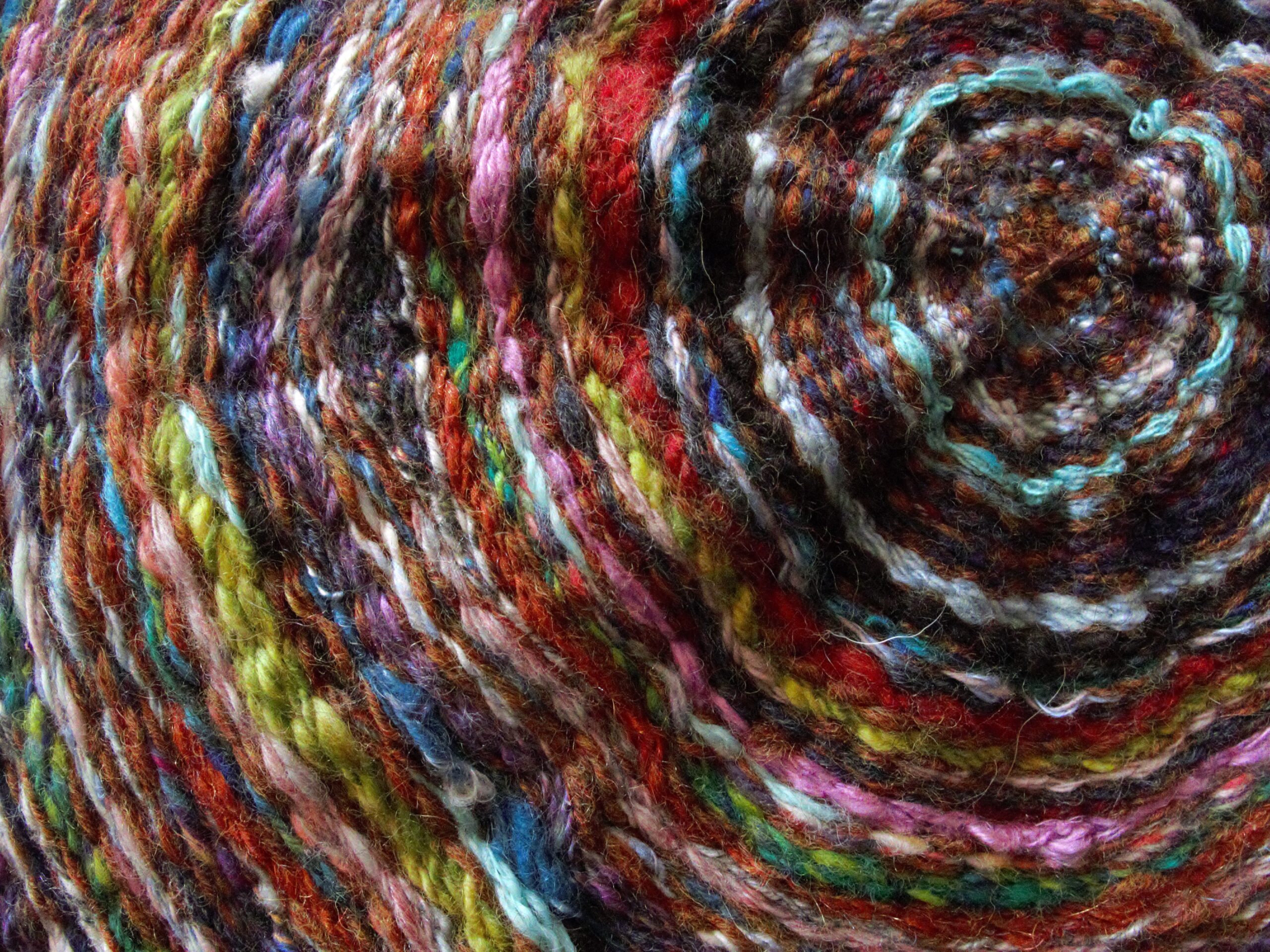 This close-up photo shows part of a piece of textile art. A variety of yarn colors are woven in a circular shape. The rings of color mimic the rings on a tree.