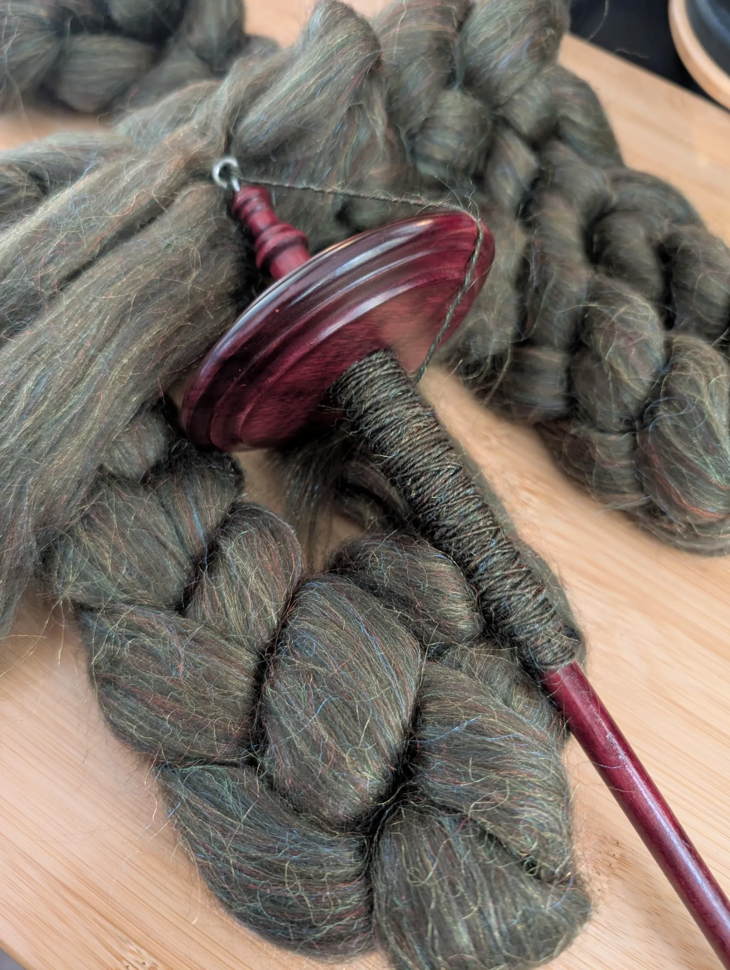 A braid of green wool fiber with flecks of nylon in it is shown on a drop spindle.
