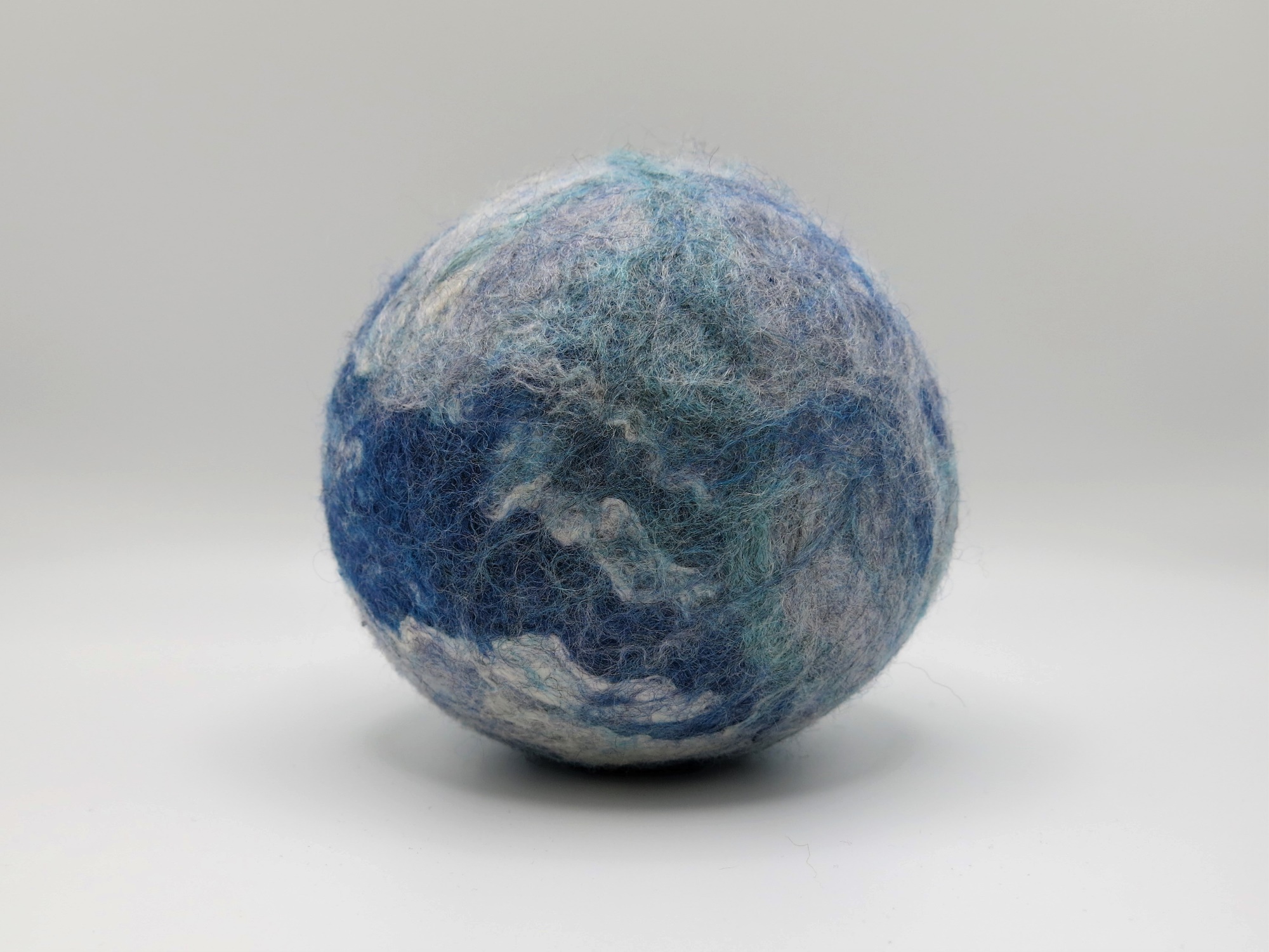 A felted ball in shades of blue, white, and green.