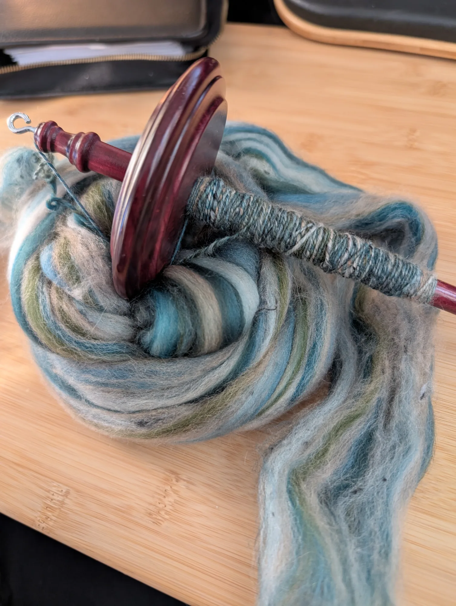 Wool and camel fiber on a drop spindle. The colors are blue, a little green, and some beige and tans.