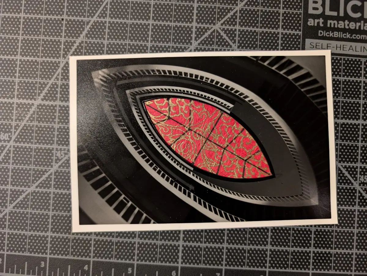 A black and white photo taken from beneath a curved, football shaped staircase at the Museum of Contemporary Art Chicago rests on a cutting mat. The center of the photo has been cut out, and a red floral paper has been put in its place.