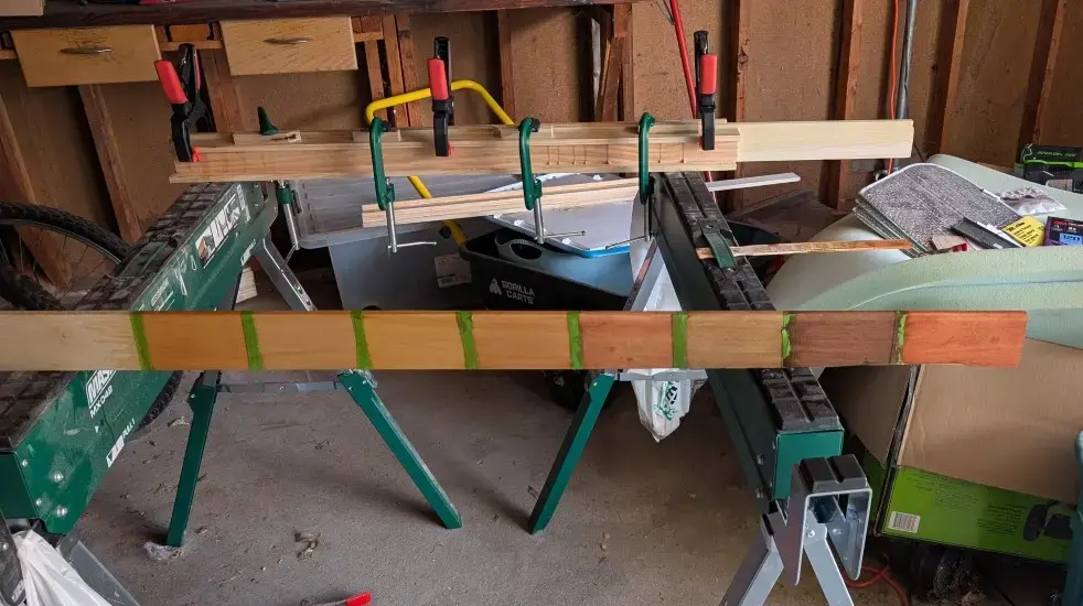A wooden board shows eight different colors of stain. Each patch of stain is separated with some painter's tape.